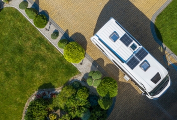 Caravana con placas solares vista desde el aire, estacionada en entorno natural.